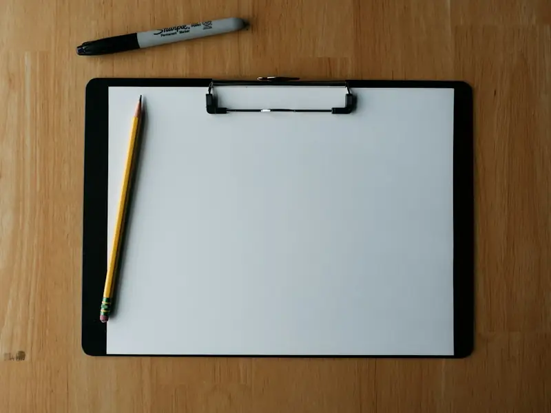 Klemmbrett mit leerem Blatt und Stift auf einem Holztisch